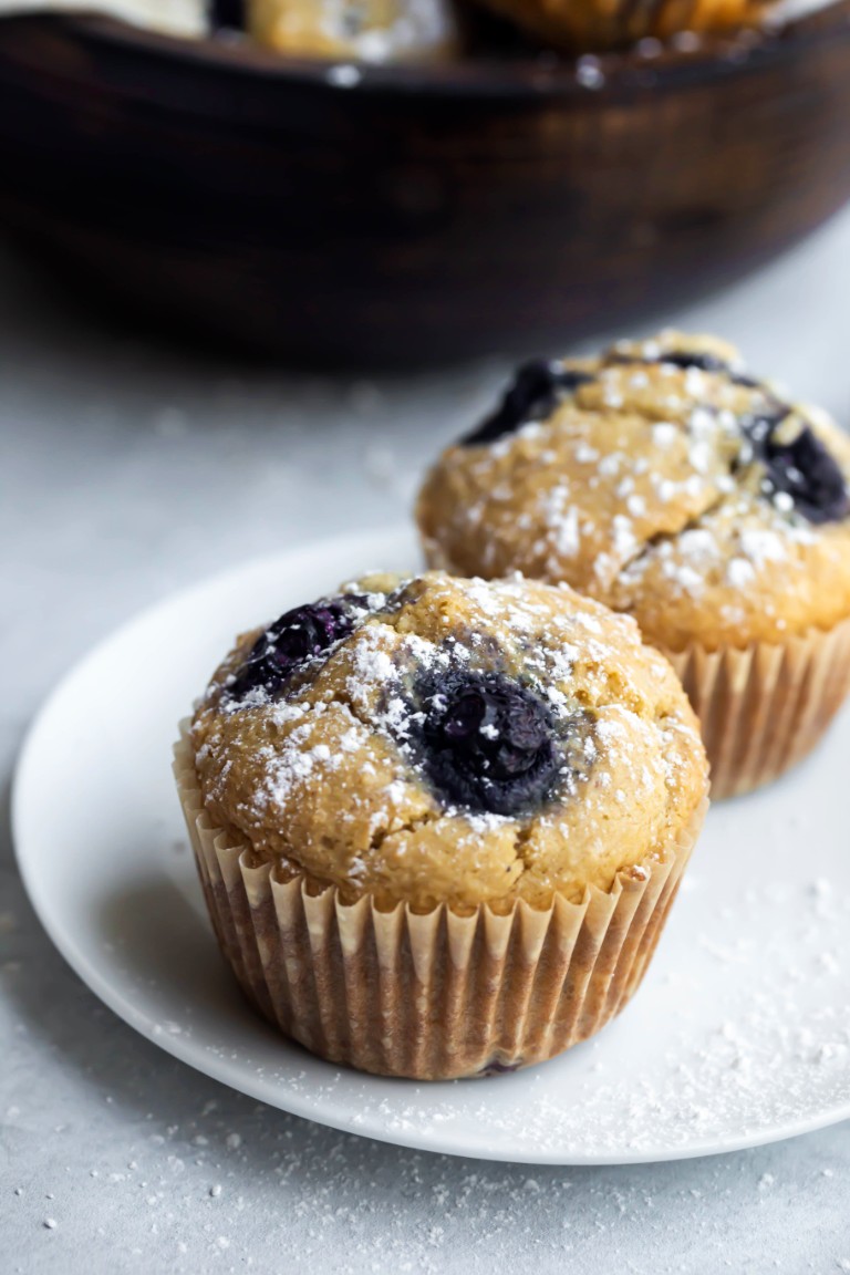 2 muffins on white plate with powdered sugar sprinkled on top