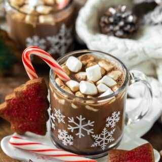 2 snowflake mugs of vegan peppermint mocha latte on wood serving platter and candy canes and cookies
