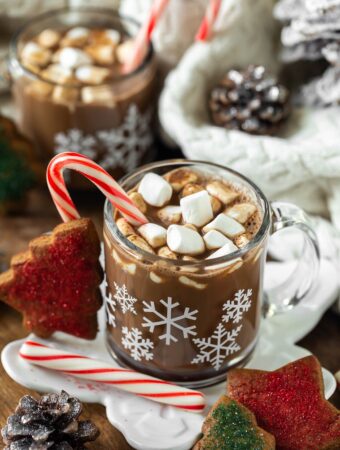 2 snowflake mugs of vegan peppermint mocha latte on wood serving platter and candy canes and cookies