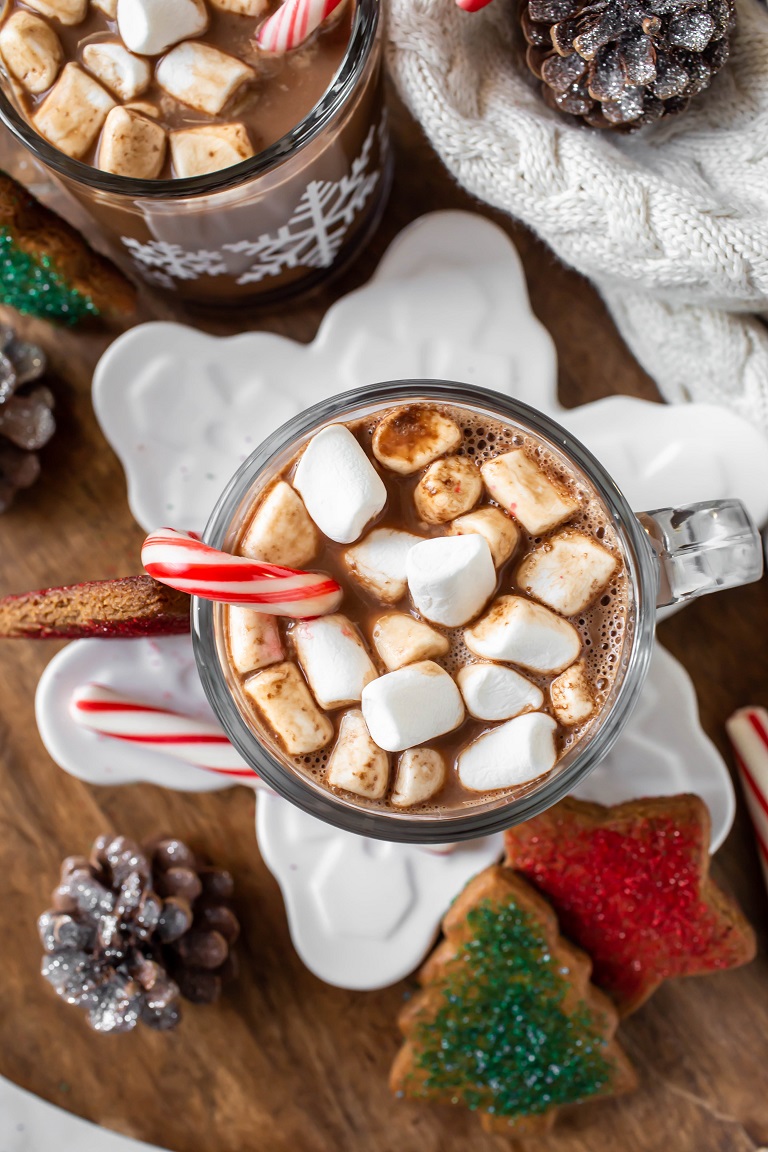overhead view of mug with marshmallows and candy cane on white snowflake plate