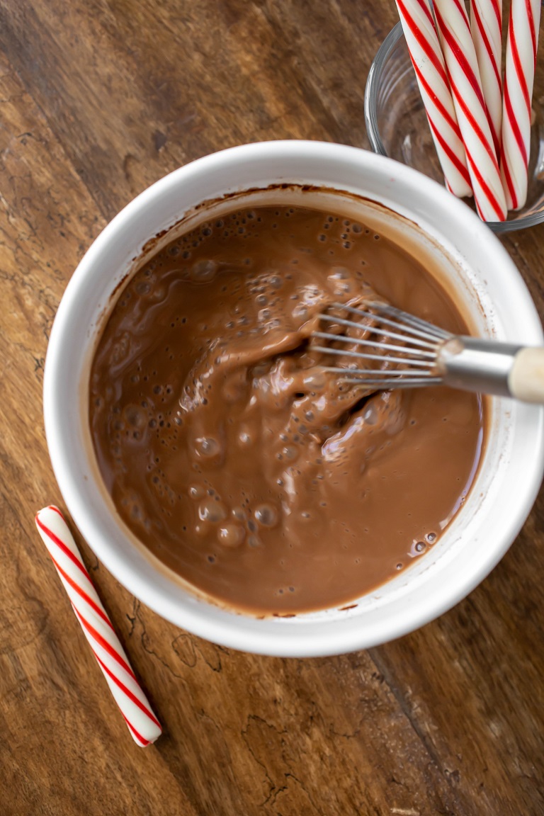 white bowl with peppermint hot chocolate with hand whisking vigorously